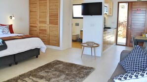 A bedroom with a bed, a wooden wardrobe, a TV, and a bathroom visible through an open door. - In peaceful Prazeres | Qta. Inácia Hibiscus Studio (Prazeres)