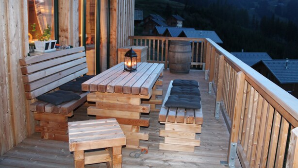 En träveranda med bänkar och bord, med utsikt över ett bergigt landskap.