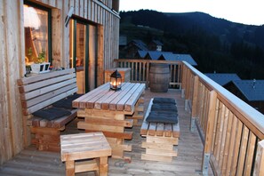 Terraza de madera con bancos y mesas, con vistas a un paisaje montañoso.