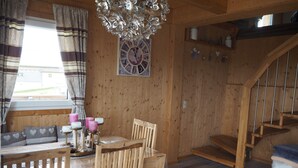 En interiör med träinredning, ett matbord, stolar, en kristallkrona, en klocka och en trappa.
