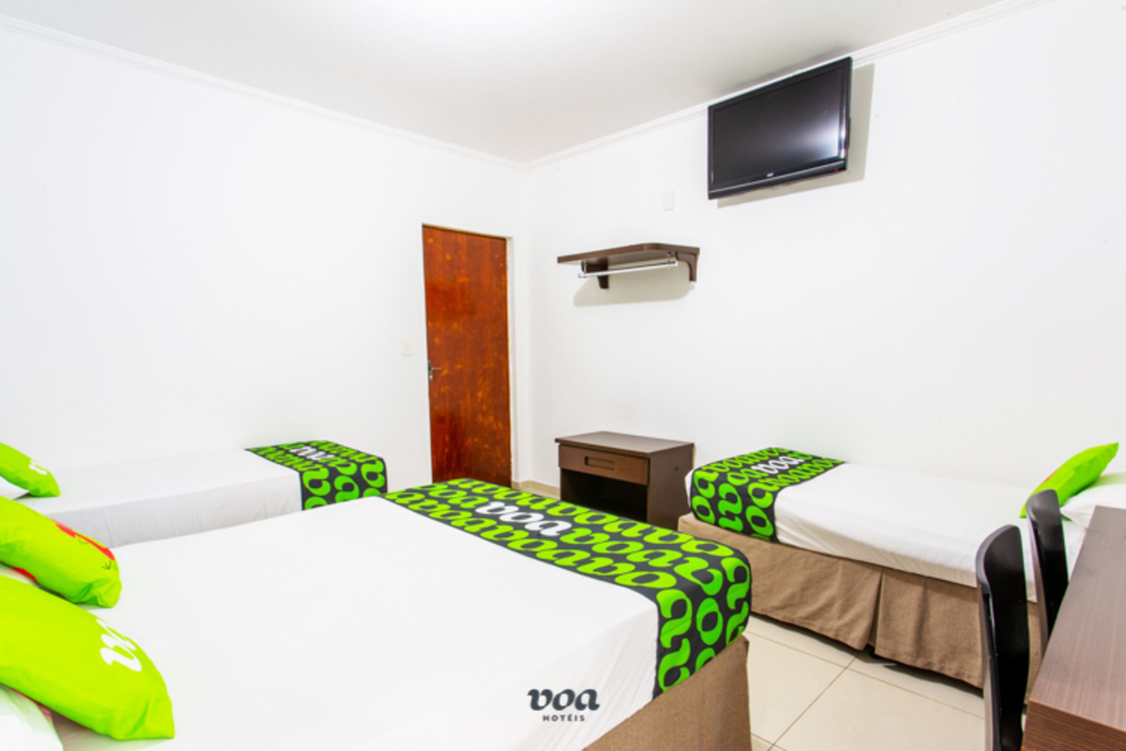 Habitación de hotel con dos camas, un televisor montado en la pared y una puerta de madera.