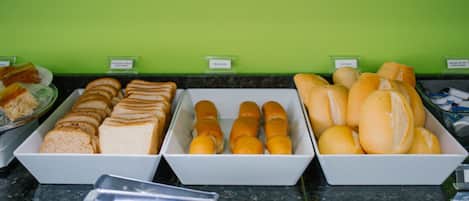 Buffet com diversos alimentos, incluindo pães, pãezinhos e doces.