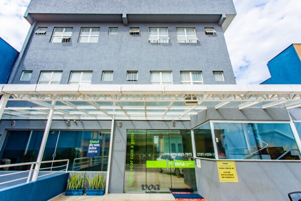 A modern hotel entrance with a glass facade, a covered entrance area, and a sign indicating room availability. - VOA Convenience Hotel (Jundiai)