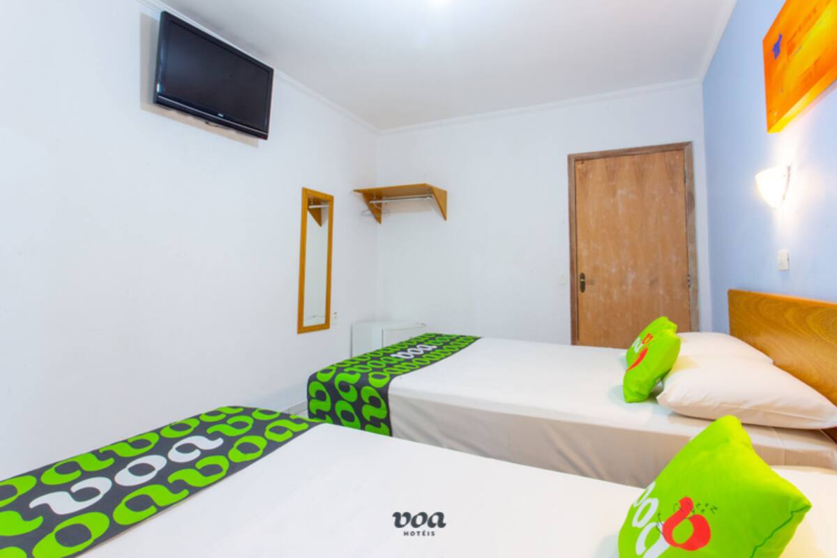 A bedroom with two beds, a TV mounted on the wall, and a wooden door.