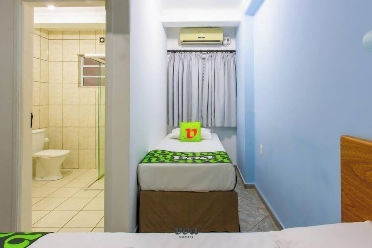 A small, narrow room with a bed, a toilet, and a shower area.
