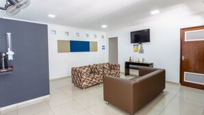 A hotel room with a sofa, a small table, a flat-screen TV mounted on the wall, and a door with a security panel. - VOA Convenience Hotel (Jundiai)