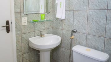 Un baño con lavamanos blanco, espejo e inodoro. Hay un dispensador de jabón verde sobre el lavamanos y una toalla blanca colgada en la pared.