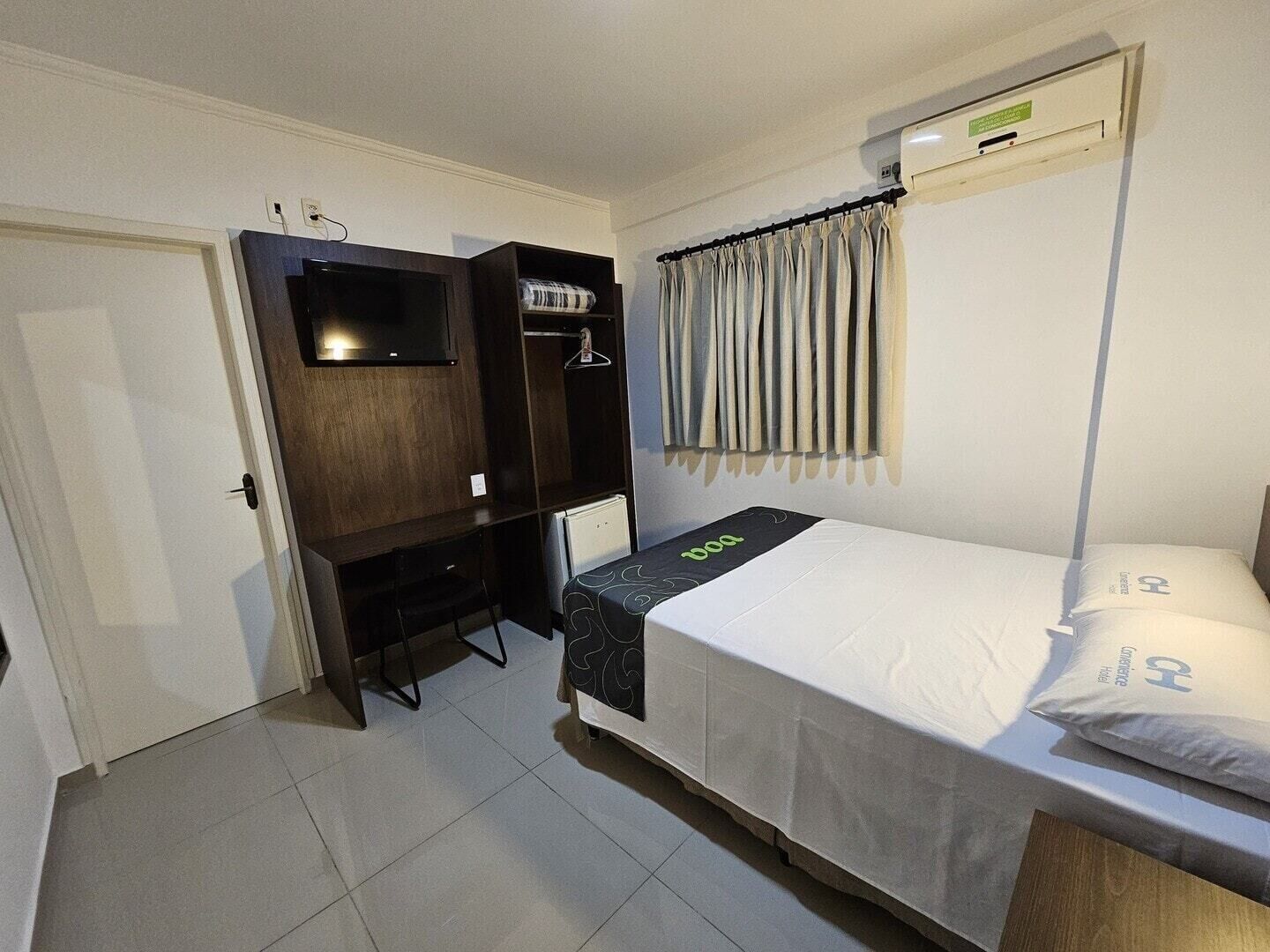 Una habitación pequeña y luminosa con una cama, un escritorio y un televisor.