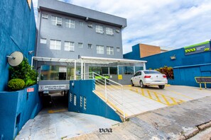 A hotel entrance with a blue wall, a white car parked inside, and a sign indicating a height limit of 2.1 meters. - VOA Convenience Hotel (Jundiai)