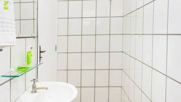 Baño con lavamanos blanco, inodoro y zona de ducha. El piso tiene un logotipo.