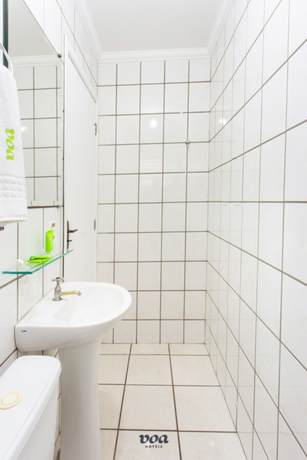 A bathroom with a white sink, a toilet, and a shower area. The floor has a logo.