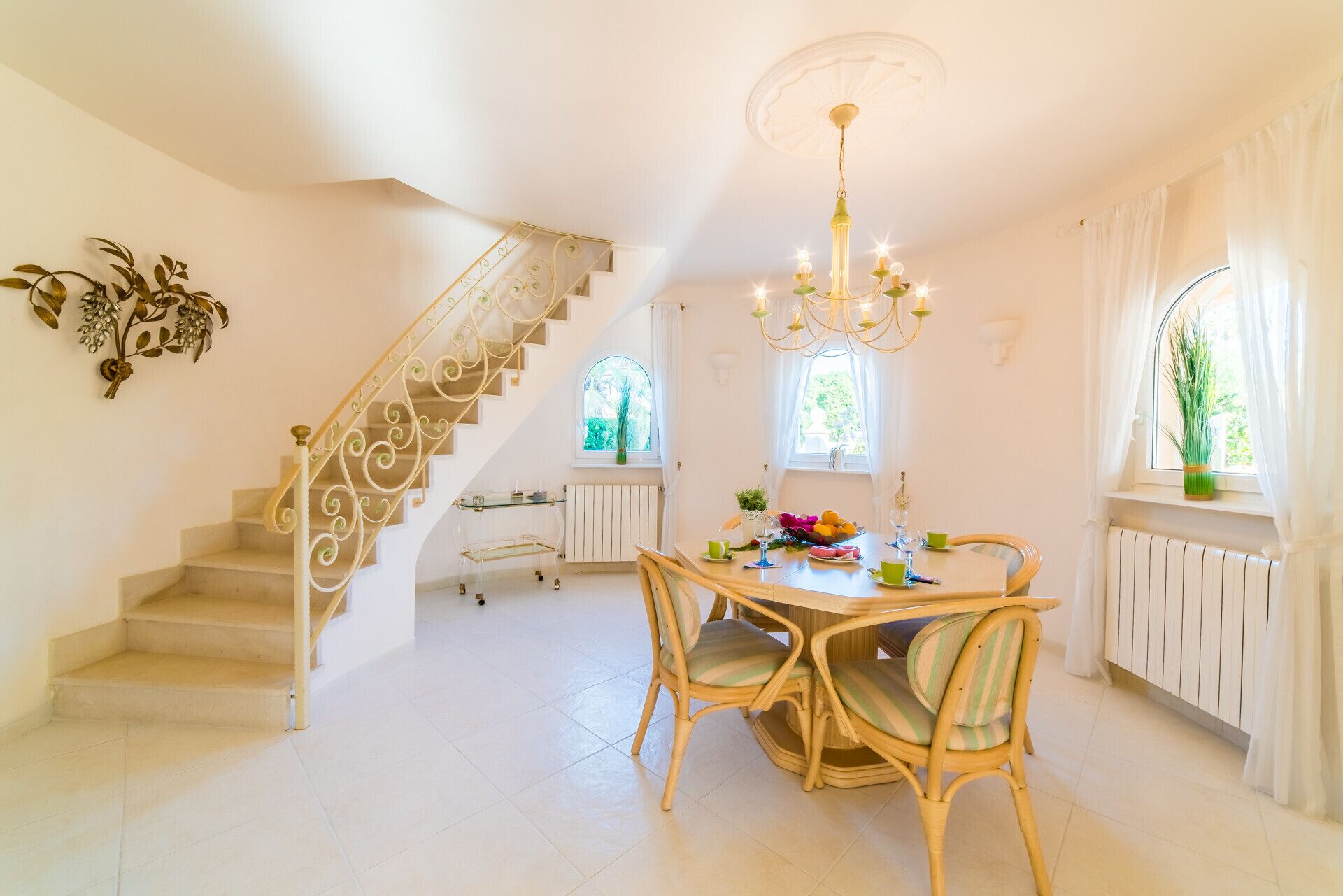 Un espace repas comprenant une table, des chaises, un lustre et un escalier agrémenté d’une rampe décorative.