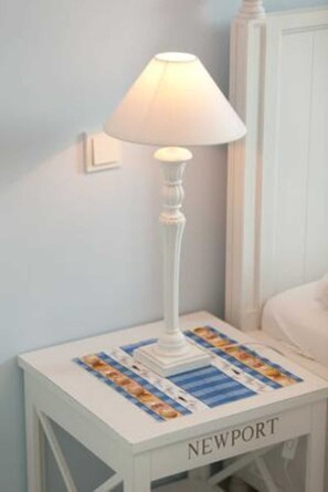 Ett vitt nattduksbord med en lampa och en underlägg med bilder från tidningar.