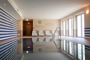 Ein moderner Poolbereich im Innenbereich mit spiegelndem Boden, Sitzgelegenheiten am Pool und großen Fenstern für natürliches Licht.