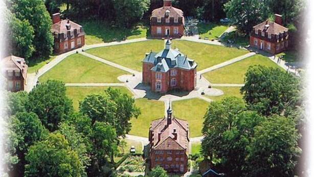 Ein Luftbild eines formalen Gartens mit symmetrischen Wegen, einem zentralen Gebäude und umliegenden Strukturen.