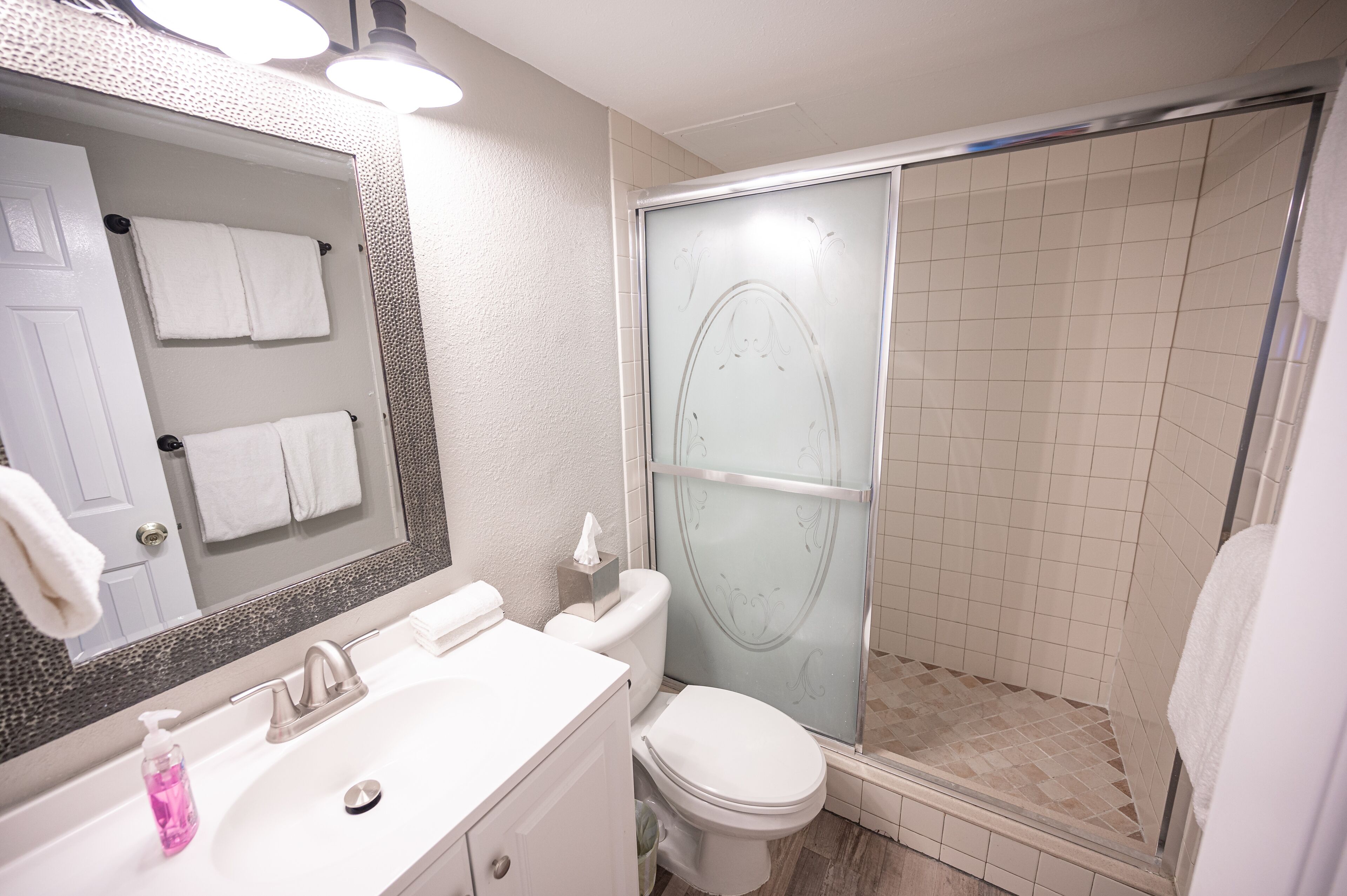 A bathroom with a white sink, a toilet, a glass shower enclosure, and a large mirror.