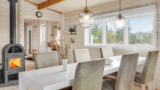 Et hyggeligt spiseområde med brændeovn, hvidt bord og stole.