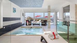 Een modern binnenzwembad met een jacuzzi, ligbedden en een glazen balustrade met uitzicht op een prachtig panorama.