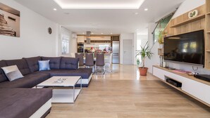 Een moderne woonkamer met een hoekbank, een salontafel en een televisie op een houten plank.