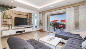 Een moderne woonkamer met een flatscreen-tv, een bank, een salontafel en een balkon met rode parasols.