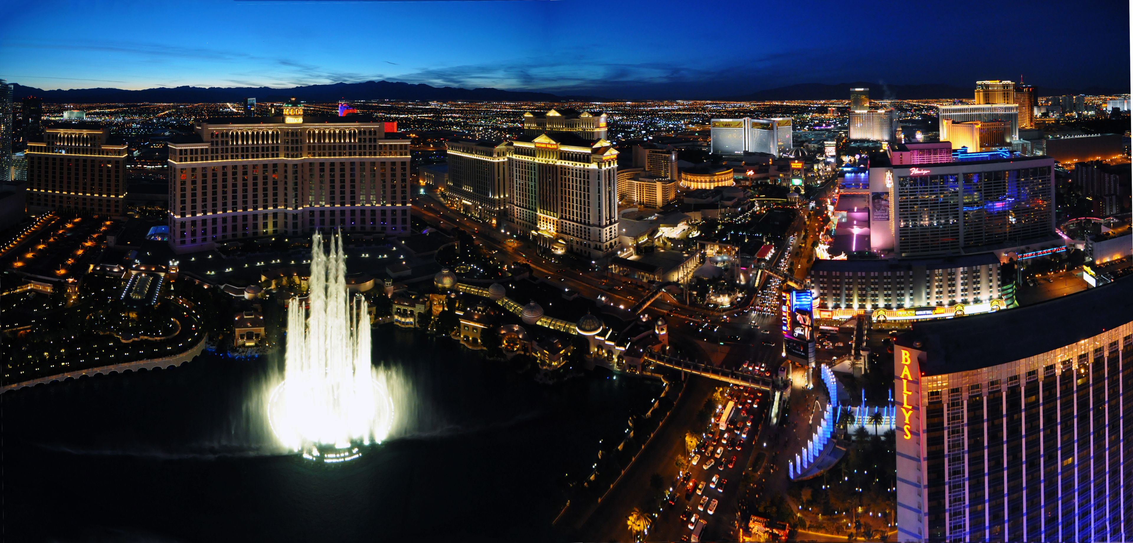 A nighttime cityscape with prominent buildings, a central fountain, and a busy street.