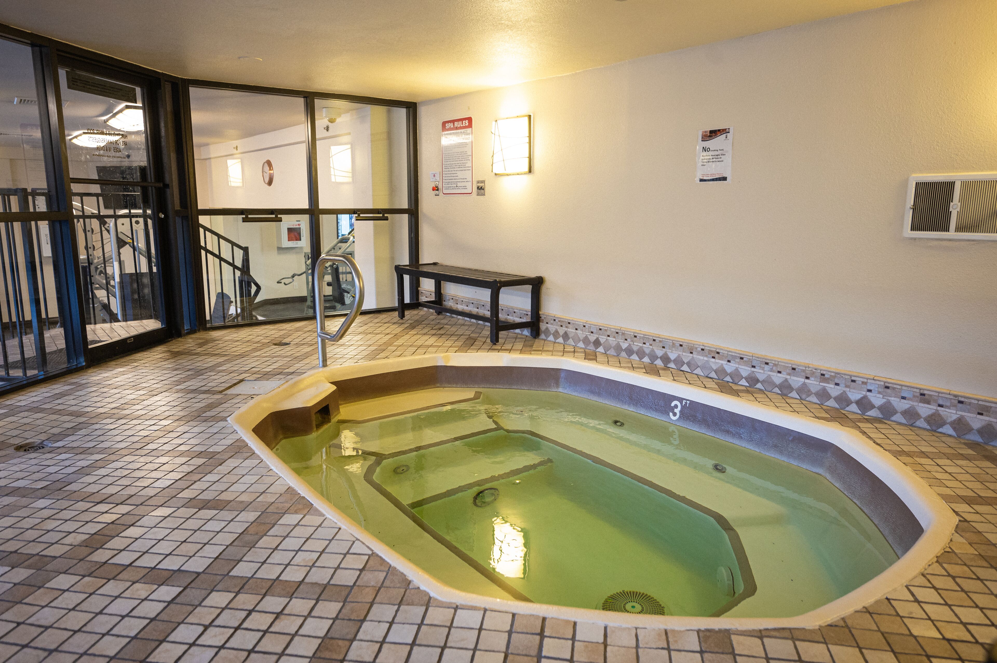 Une piscine dont le sol est carrelé, avec un banc et un escalier menant à un autre espace.