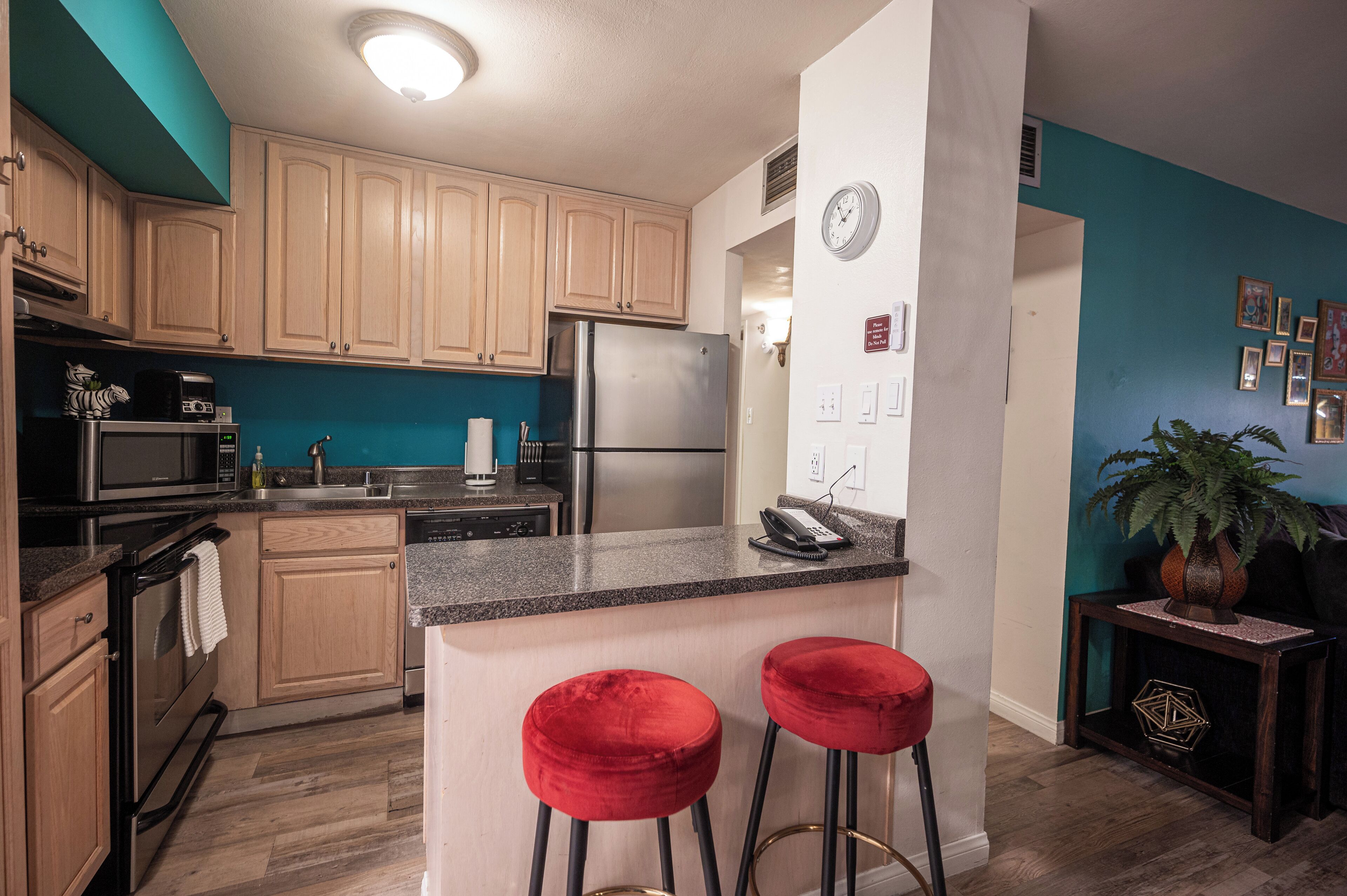 Una cocina moderna con armarios de madera, electrodomésticos de acero inoxidable, encimera de granito y dos taburetes rojos.
