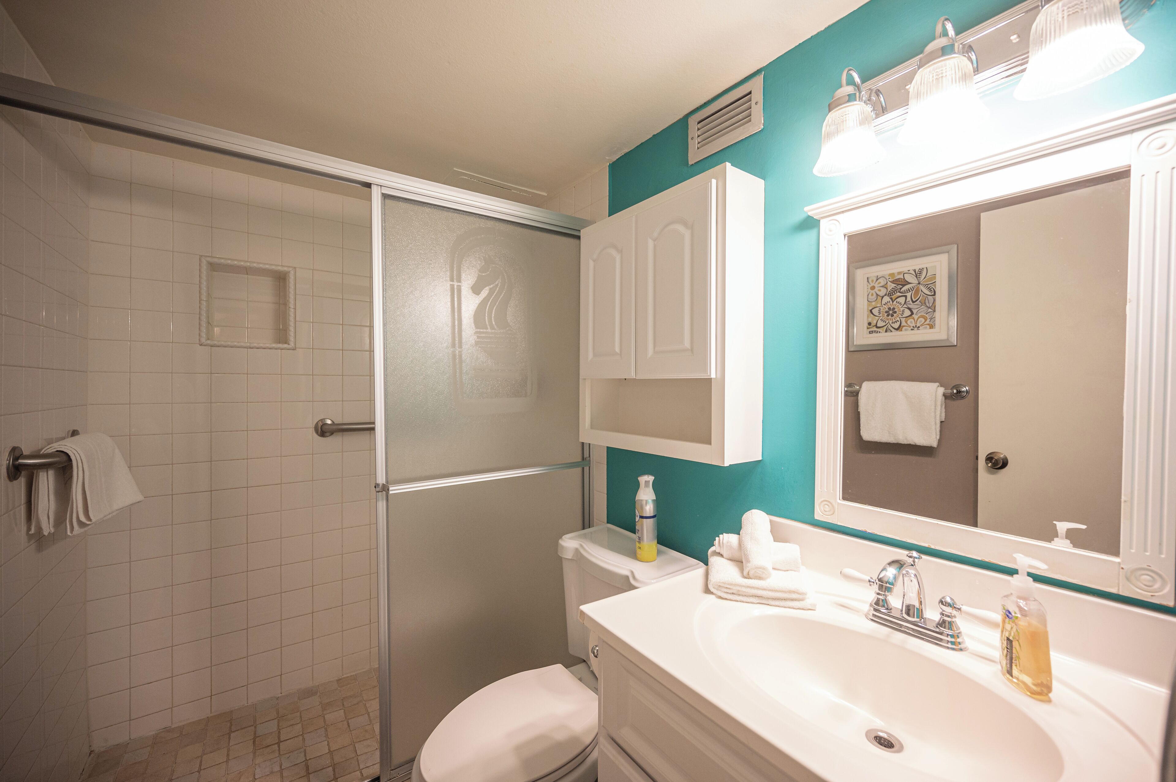 A bathroom with a shower, toilet, sink, and a mirror.