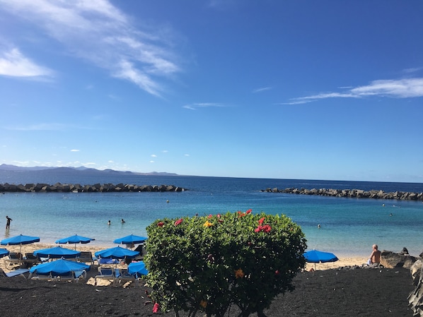 A beach with blue umbrellas, a black sand area, and a clear blue sky. - Exclusive location, Playa Blanca, heated pool, sea views, near the beach, WiFi (Playa Blanca)