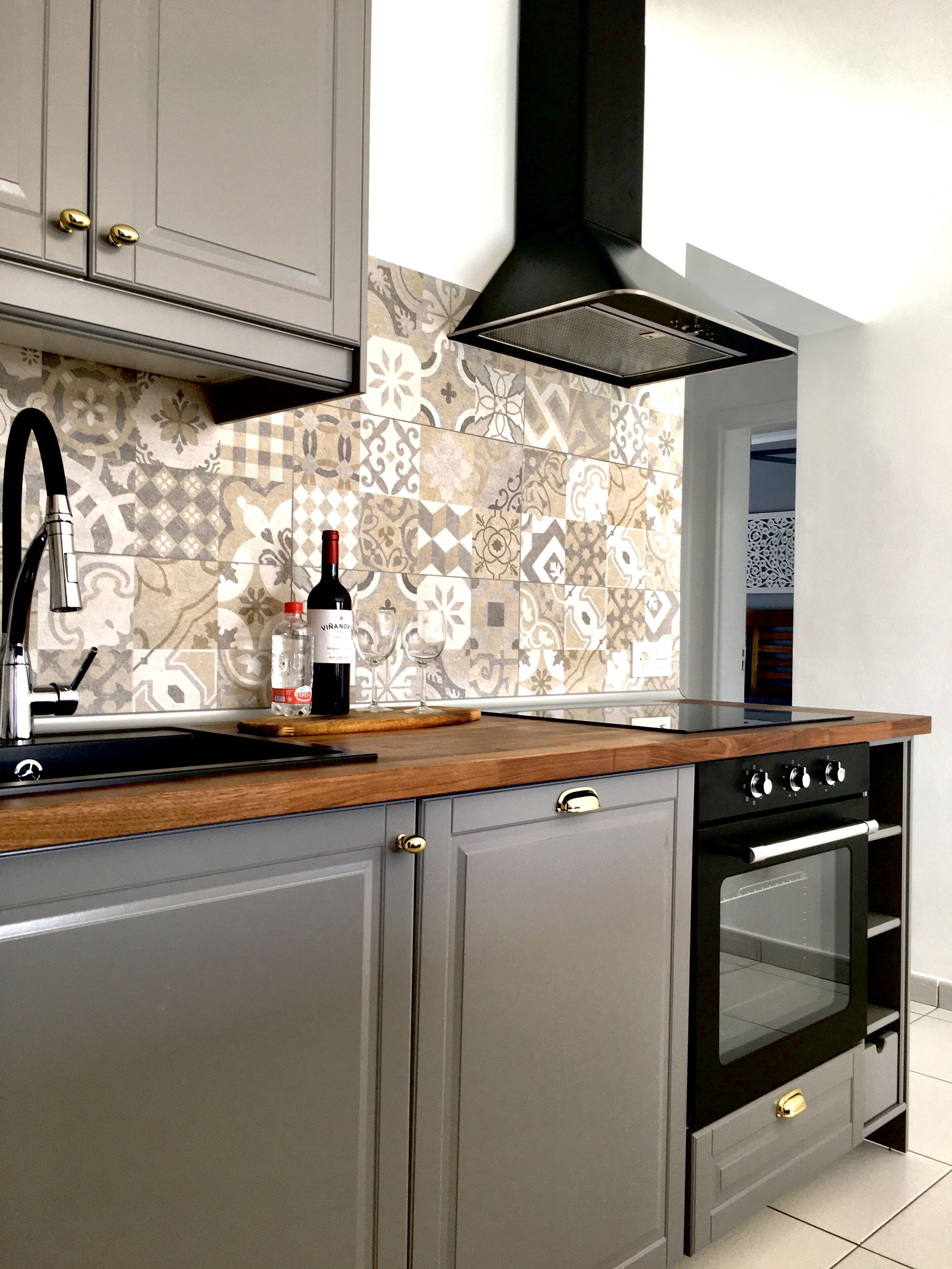 A kitchen with grey cabinets, a black range hood, a patterned backsplash, and a wine bottle on the counter.