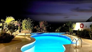 Ein Schwimmbecken mit bogenförmigem Design, umgeben von Pflanzen und einem Rettungsring an einer Wand.