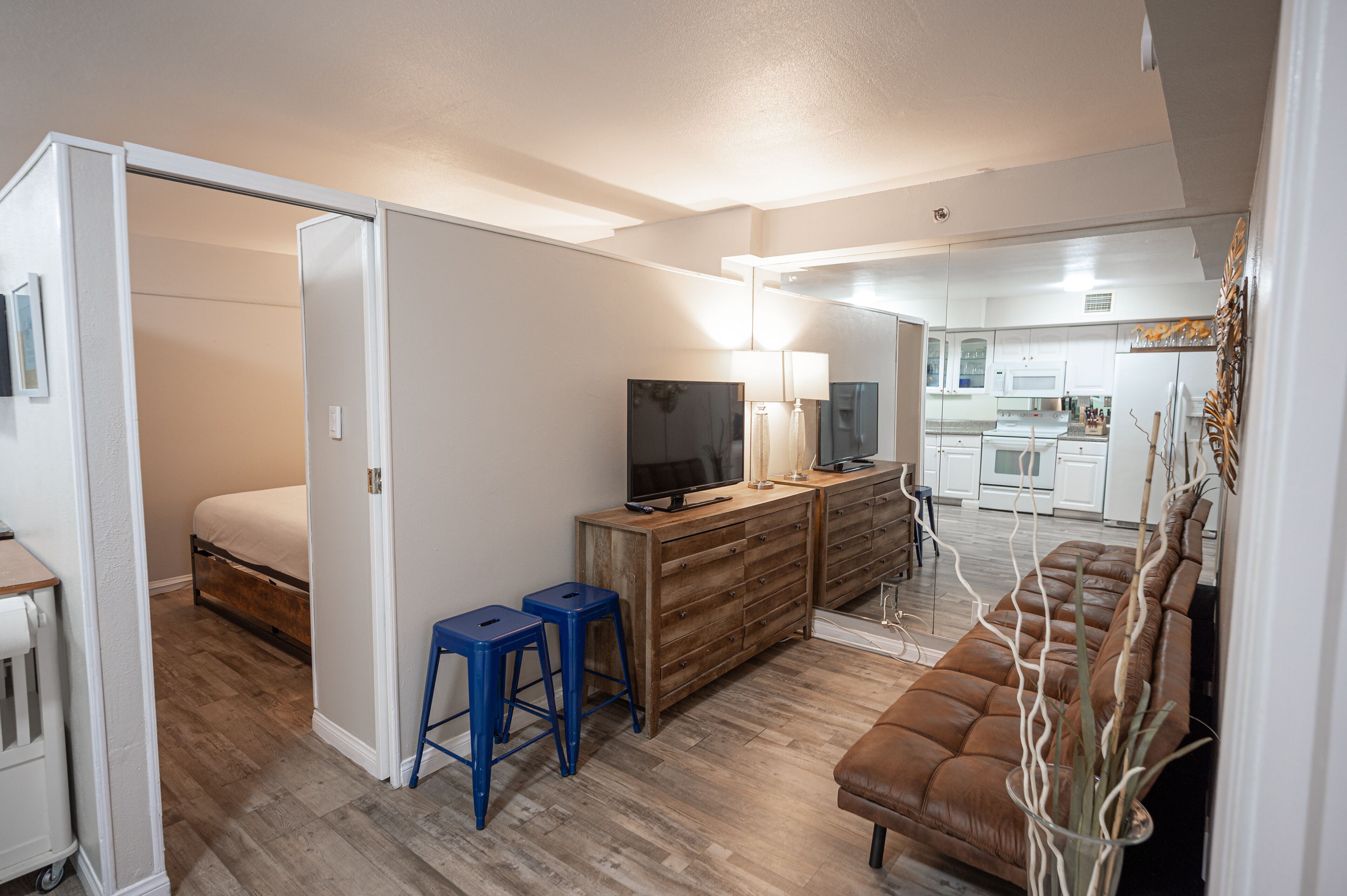 A compact living space with a bed, a TV, a wooden dresser, and a brown sofa.