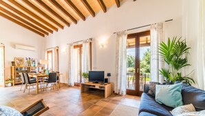 A spacious living area with a wooden ceiling, a dining area with a table and chairs, a television, and a large window with curtains.