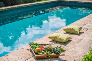 A swimming pool with a fruit basket and two pillows on the edge.