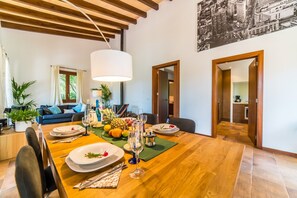 A dining area with a wooden table set for a meal, a sofa in the background, and a cityscape mural on the wall.
