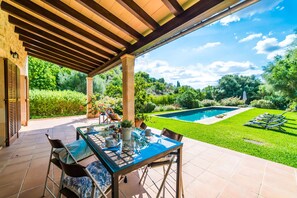 Une terrasse extérieure avec une table et des chaises en verre, une piscine et un jardin bien entretenu.