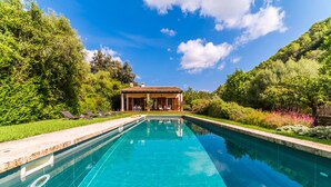 A swimming pool with lounge chairs, a covered seating area, and lush greenery surrounding the pool.