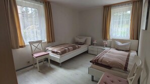 Een slaapkamer met twee bedden, een stoel, een nachtkastje en een raam.