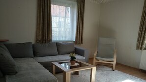 Een woonkamer met een grijze modulaire bank, een houten salontafel met een plant, een blauwe fauteuil en een wit vloerkleed.
