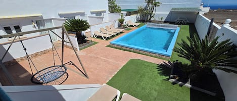 Una piscina en la azotea con un columpio, sillones de descanso y césped artificial.