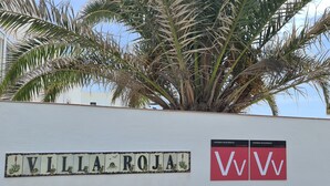 En vägg med namnet ”VILLA ROJA” och två skyltar med texterna ”VV” och ”VIVIENDA VACACIONAL”.
