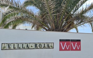 Een muur met de naam 'VILLA ROJA' en twee borden met de tekst 'VV' en 'VIVIENDA VACACIONAL'.