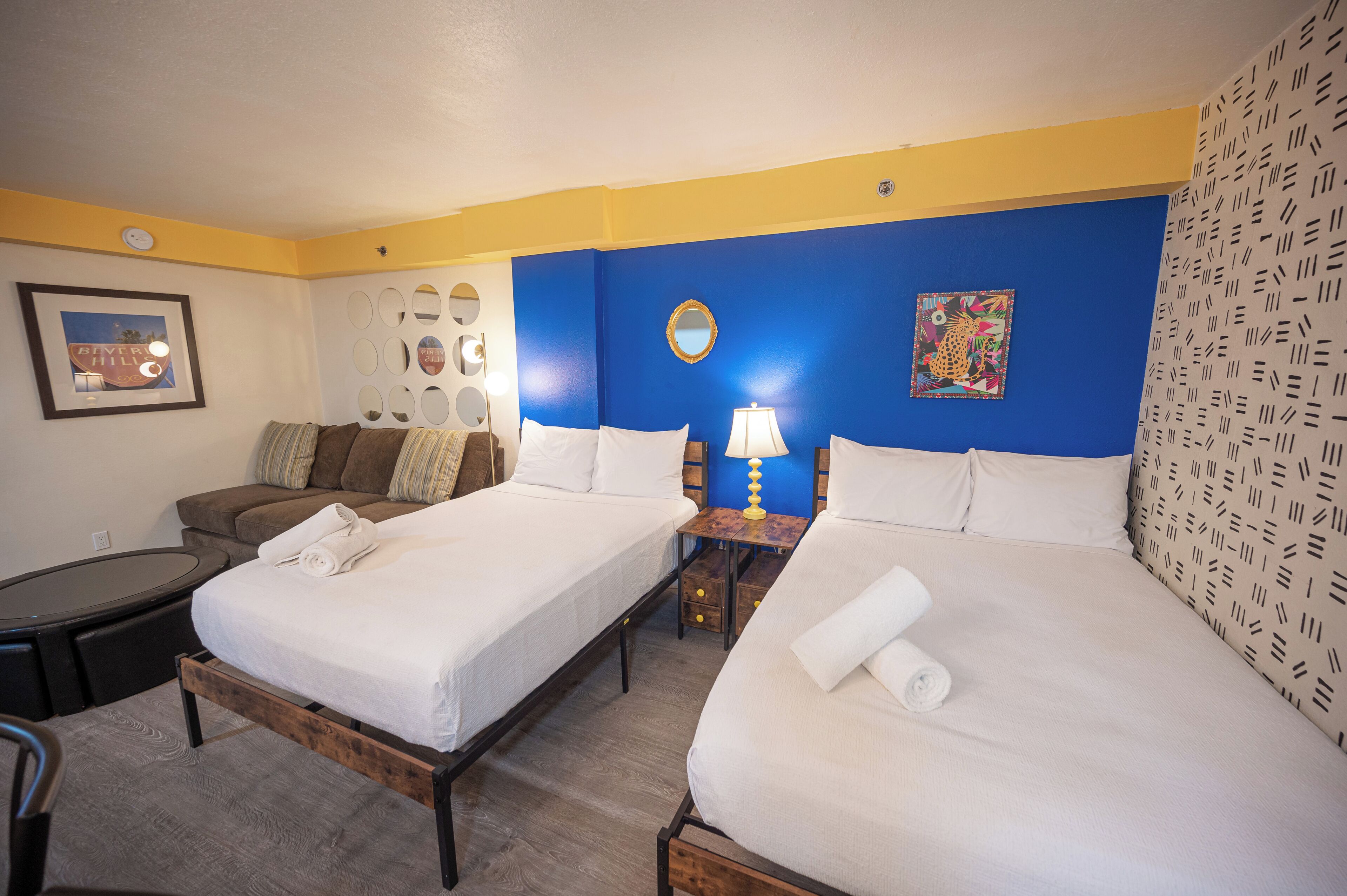 Une chambre d’hôtel avec deux lits, un canapé, une petite table avec une lampe et un miroir au mur.