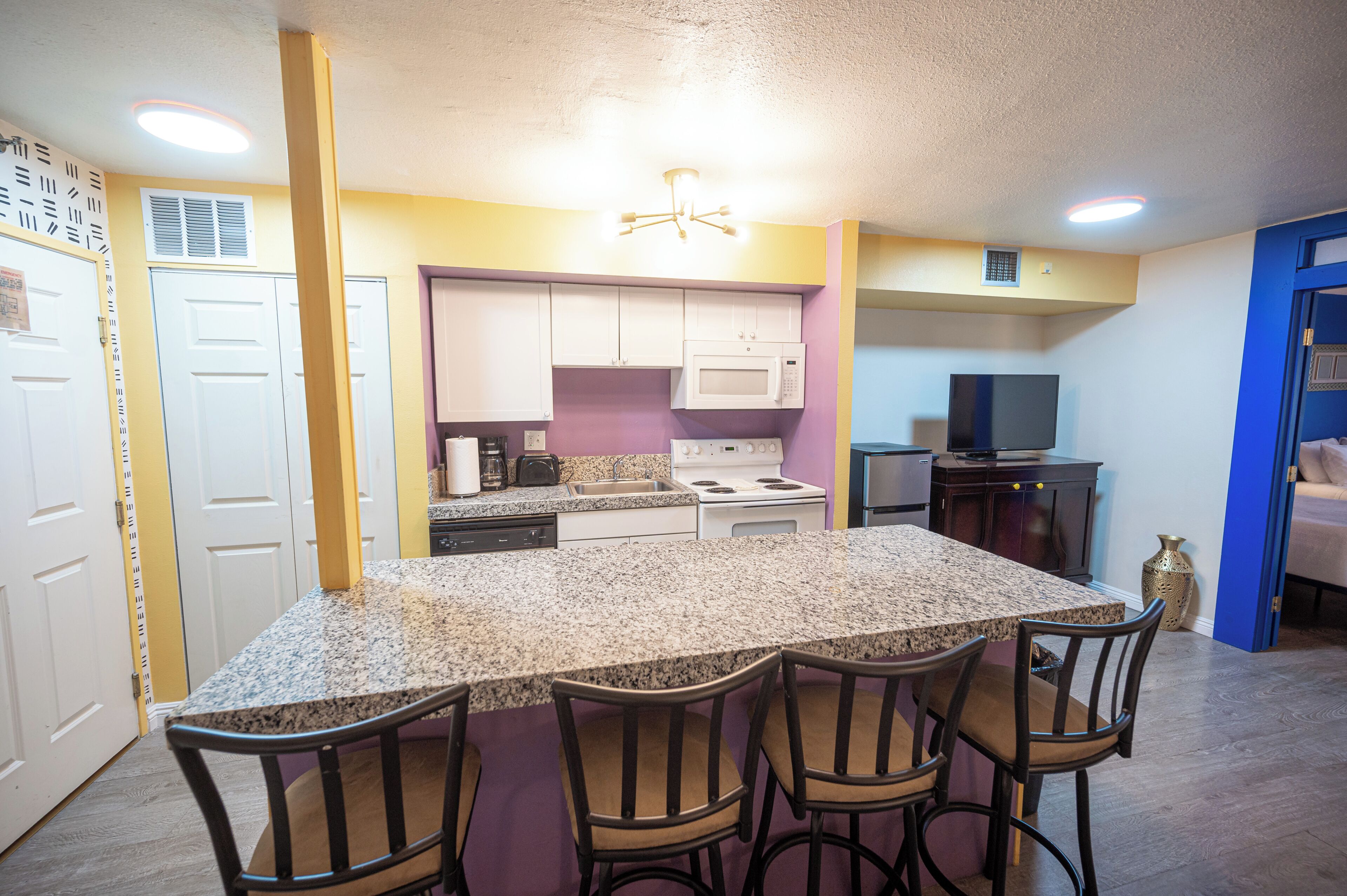 A kitchen with a granite countertop, white cabinets, a microwave, stove, and a TV.