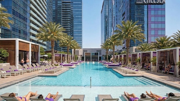 A pool area with lounge chairs, palm trees, and modern buildings in the background. - Stay Together Suites | Cozy Strip Condo (Las Vegas)