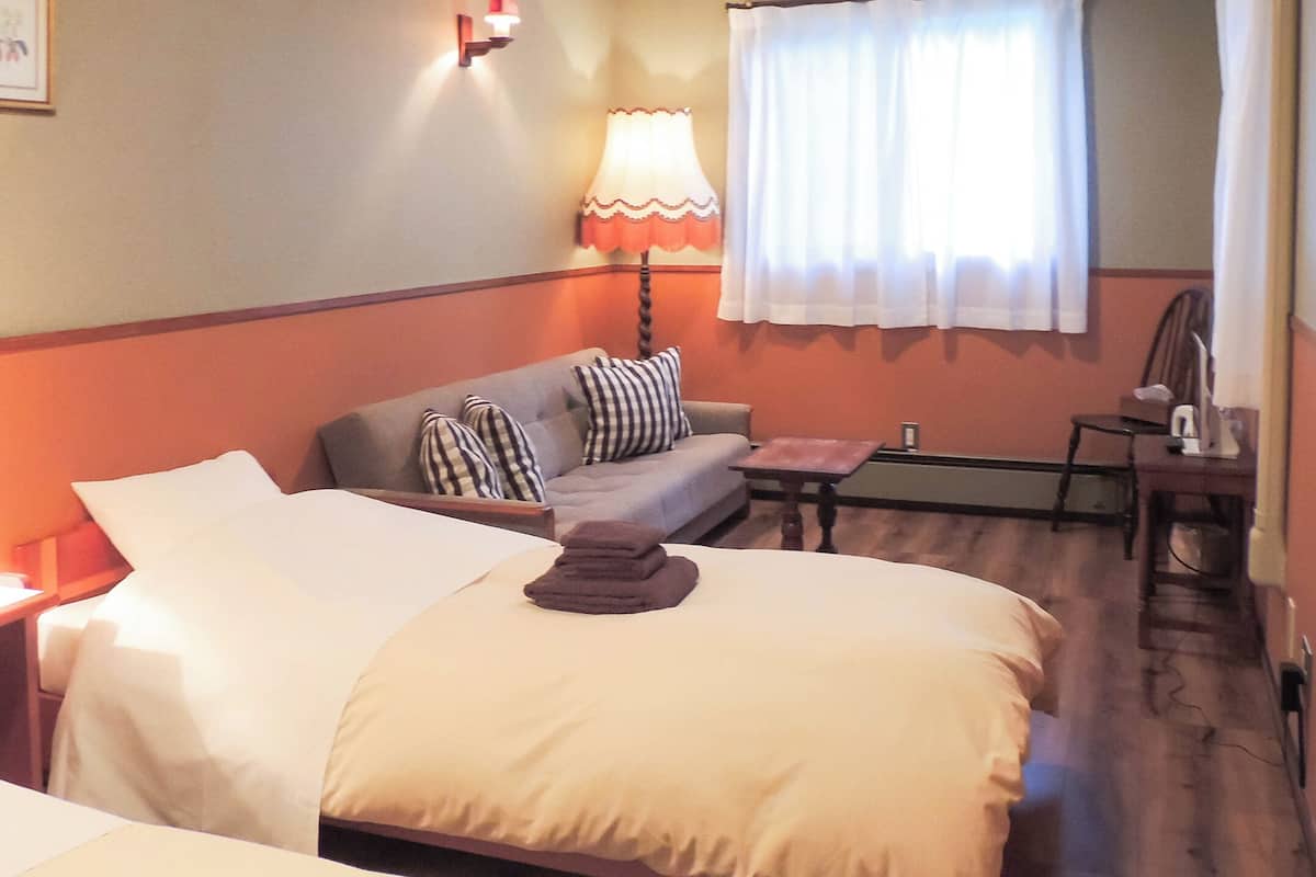 A hotel room with two beds, a sofa, a small table, and a lamp.