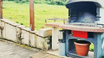 Un horno exterior de piedra con un compartimento rojo, un recipiente metálico y un banco de madera.