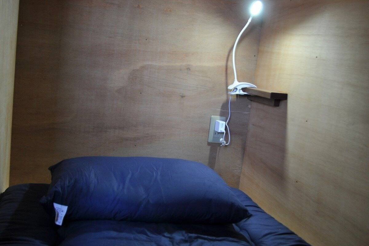 A single bed with a blue mattress and pillow in a room with wooden walls and a wall-mounted light fixture.