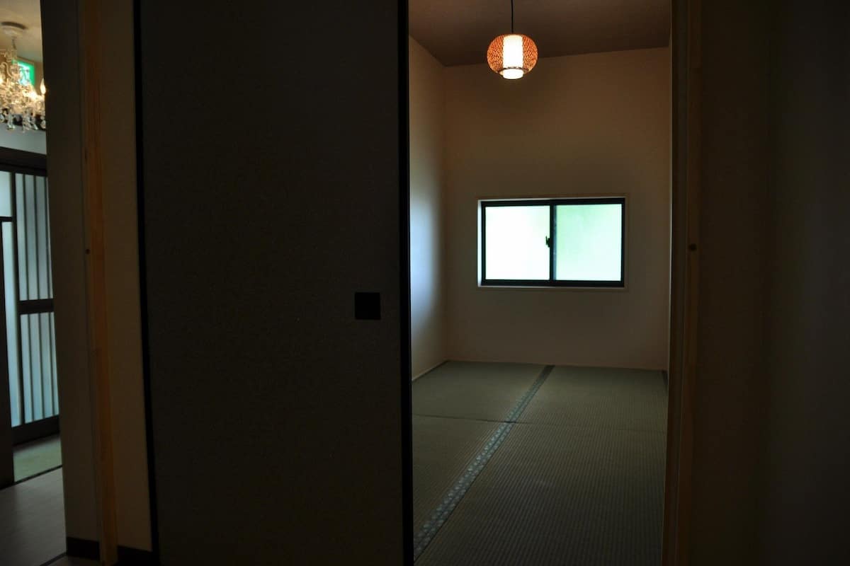A room with tatami flooring, a sliding door, a window with a view, and a hanging light fixture.