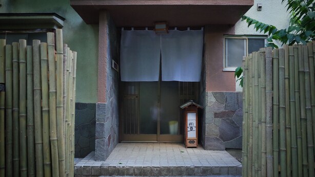 A traditional Japanese entrance with a wooden gate, a stone wall, and a small wooden structure. - chambre d'hôte TATAMI - Hostel (Suwa)